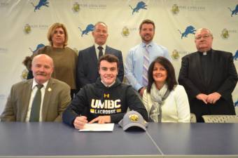 Pope John senior Dane Armstrong signs his National Letter of Intent for lacrosse at the University of Maryland. Next to Armstrong are his parents, Keith and Renae. Back row: Athletic Director Mia Gavan, Principal Gene Emering, boys lacrosse head coach Chris Hoffmann, and Pope John President Rev. Msgr. Kieran McHugh.