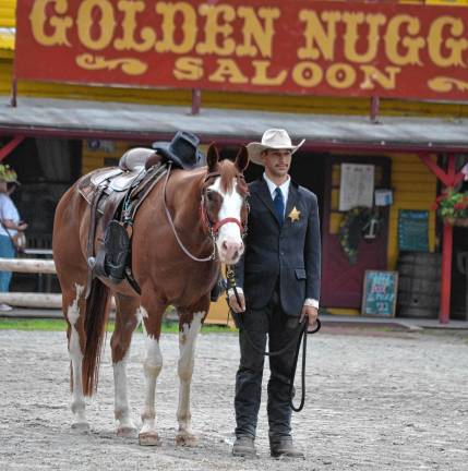 Wild West City remembers ‘Pony Bob’ Cowboy Gabe Wellington stands next to Ranger carrying an empty saddle, boots reversed in the stirrups and Robert ‘Pony Bob’ Erven’s hat on the pommel. This horse, who joined Wild West City this season, was named for Erven’s favorite quarterhorse. (Photo by Jane Primerano)