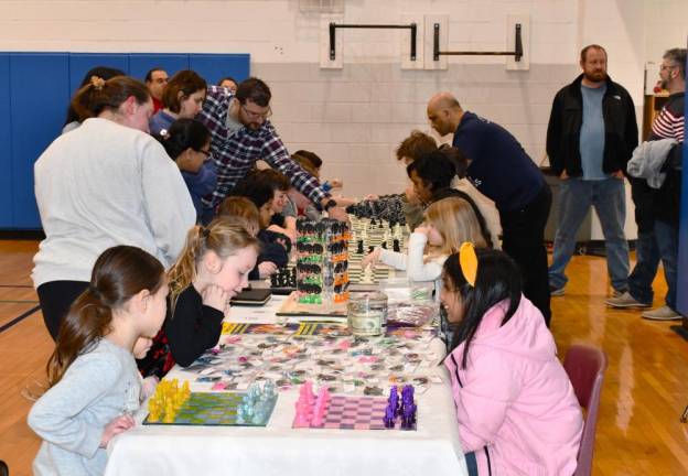 Children play chess at a long table.