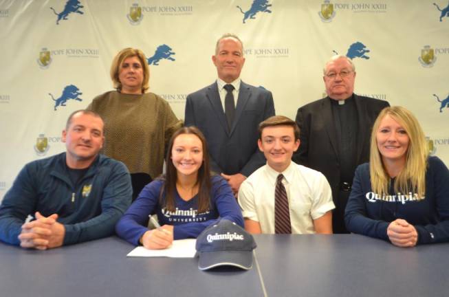 Gianna Burrini signs her National Letter of Intent for acrobatics/tumbling at Quinnipiac University. Seated next to Burrini are her parents, Jesse and Nichole, and her brother, Jesse. Back row: Athletic Director Mia Gavan, Principal Gene Emering, and Pope John President Rev. Msgr. Kieran McHugh.