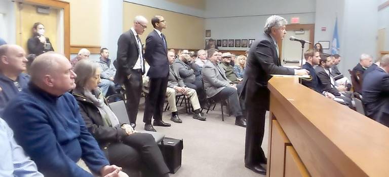 Left to right, standing: attorneys Clark and Dash listen while attorney Lawrence Cohen speaks. Just beyond the rail to the right sits the developer’s team. (Photo Frances Ruth Harris)