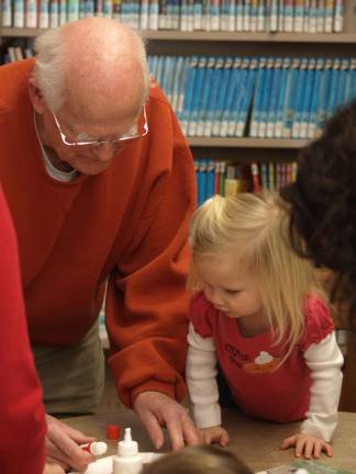 Roger Lussier of Sparta and his granddaughter Abigail Conover, 2 and a half, of Chester get to work assembling an Elmo puppet Friday morning in the Sparta Library.