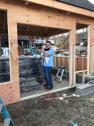Adam Anderson holds his son, Drew, who has been diagnosed with Tay-Sachs. Behind them is the enclosed hot tub area which is under construction and will provide therapy for Drew.