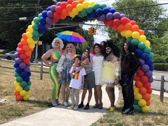 Drag performers pose for a photo under a rainbow of balloons.