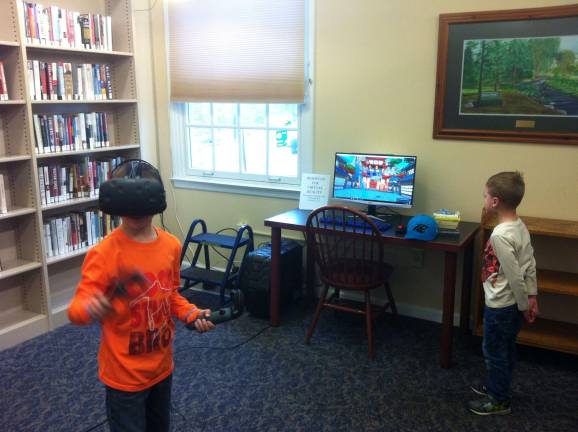 Sam Deeney, in the orange shirt, is playing Fruit Ninja in VR while brother Calvin watches the monitor