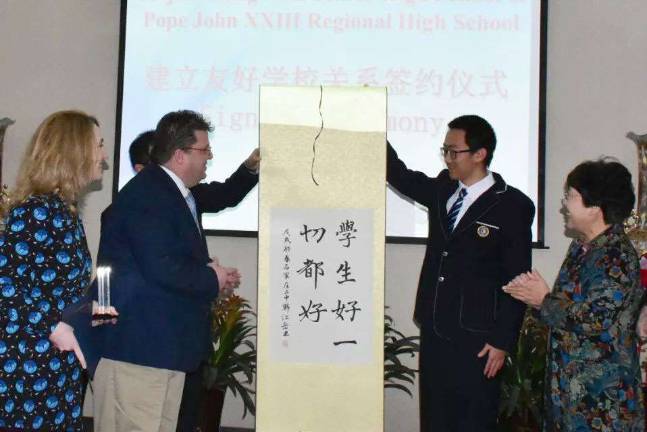 Pope John XXIII Regional High School Cultural Exchange Program Director Mary Alice Campbell and Vice President for Institutional Advancement Craig Austin, first and second from left, receive a scroll from Shijiazhuang No. 2 Middle School Superintendent Ms. Xizhen Shao, far right, and a Shijiazhuang No. 2 Middle School student after the two schools signed an agreement to become partner schools during a signing ceremony in late March at Shijiazhuang No. 2 Middle School in Shijiazhuang, China. photos provided