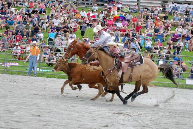 A competitor reaches for the calf during the steer wrestling contest. In the background rodeo clown Hollywood Harris (Cliff Harris) looks on. Photos by George Leroy Hunter