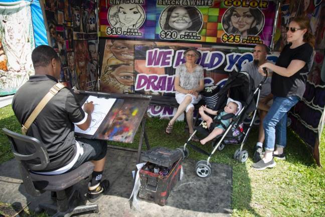 A family sits for a caricature by Tier Gaither of Decatur, Ga. From left are Lubby Mumoli, Joseph and Rosalyn Velez, and their daughter Rosella, 8 months, all of Little Falls. (Photo by John Hester)