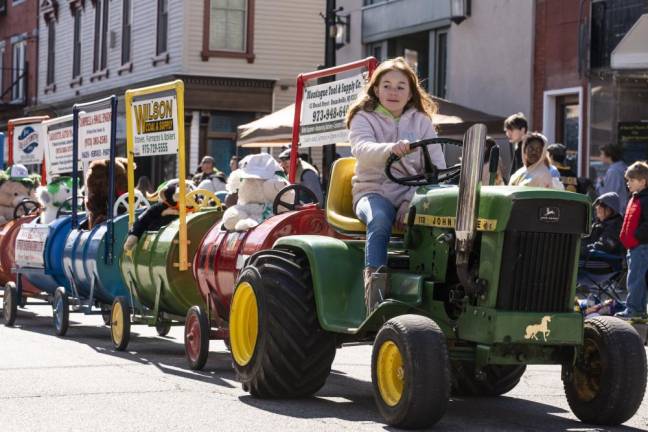 A girl drives a tractor pulling cars advertising local companies.
