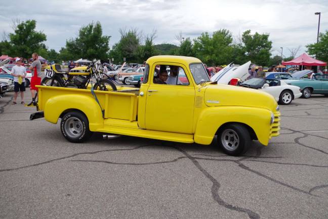 A classic yellow Chevy pickup truck hauling a color coordinated motorcycle is on the move.