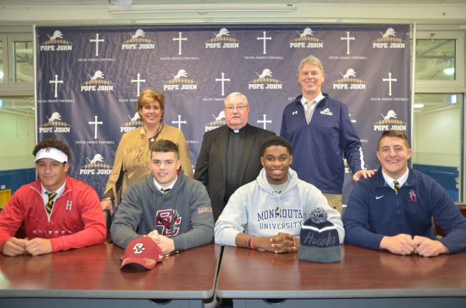 Sitting from left, Pope John XXIII Regional High School seniors Jake Brown, Nick DeNucci, Jhadir Charles and Aidan Murray pose for a picture after signing their national letters of intent on Wednesday to play NCAA Division I football for Harvard University, Boston College, Monmouth University and the University of Richmond, respectively. Standing behind the players, from left, are Pope John Athletic Director Mia Gavan, Pope John President and Principal Monsignor Kieran McHugh and Pope John head coach Brian Carlson. Photo by Anthony Spaulding, Director of Communications/Pope John XXIII Regional High School