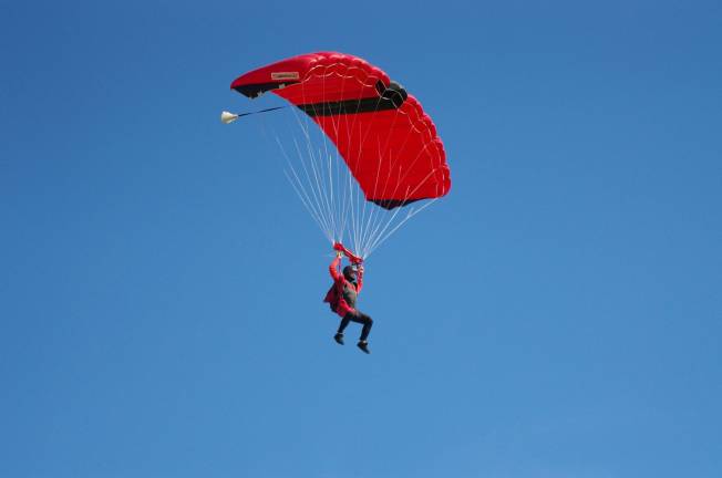 The vibrant red color of this skydiver's gear stands in sharp contrast against the blue sky.