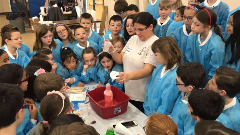 Shannon Gunter, an employee of Bayer standing in center, shows Reverend Brown fourth-grade students how to mix yeast and hydrogen peroxide to form &quot;Elephant Toothpaste&quot; during STEM Day on Friday at Reverend George A. Brown Memorial School in Sparta.